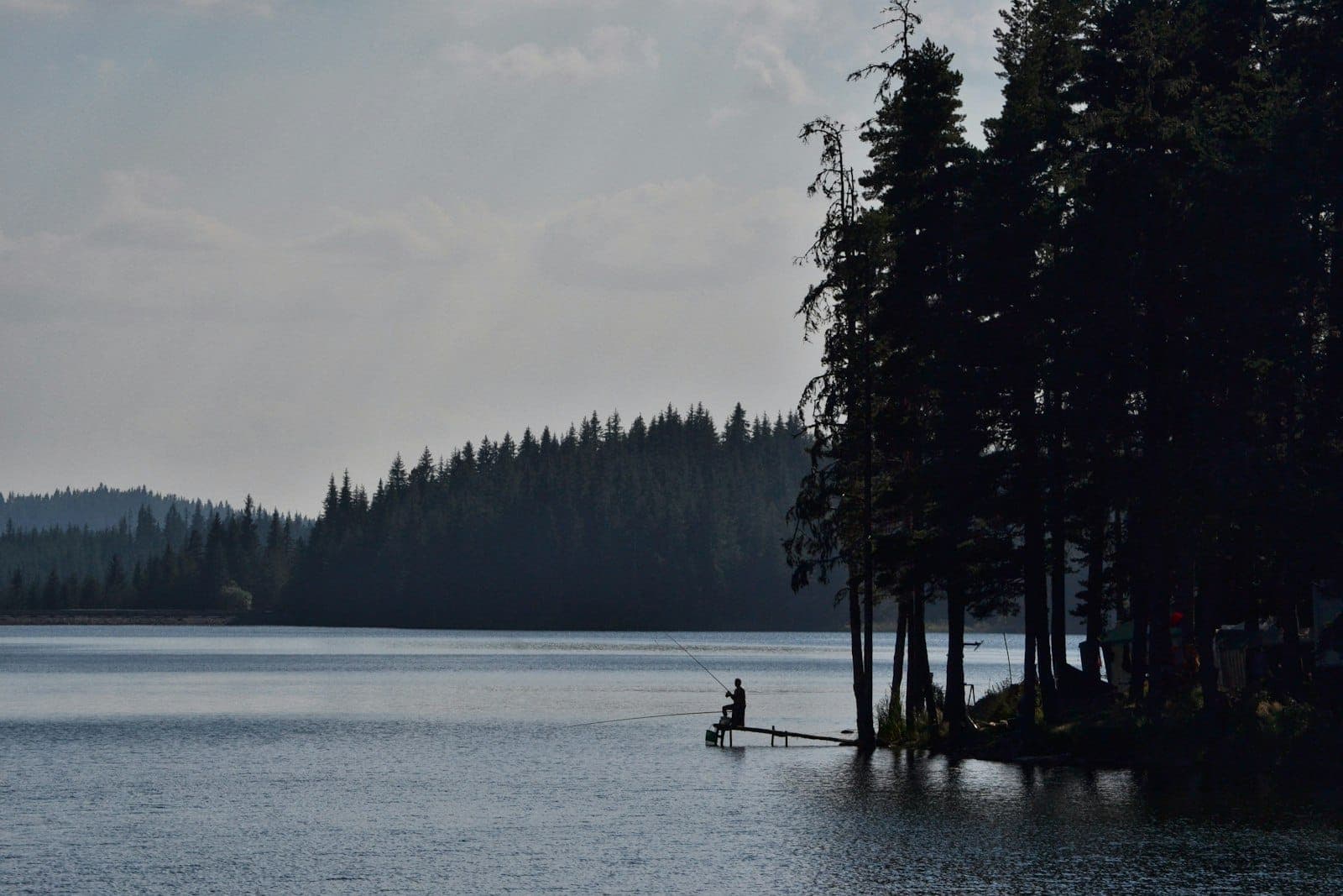 A man fishing on a quiet lake, evoking the lonely solitude in Jeannette Haien's The All of It prose passage.