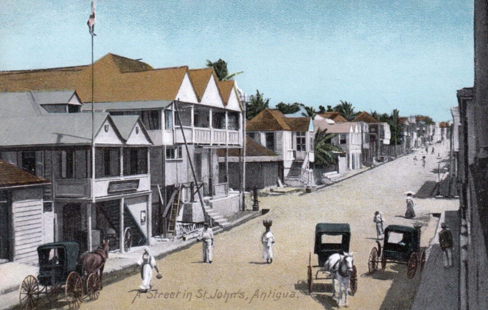 Hand-colored postcard of a street in St. John's, Antigua, around 1910, where a woman carries a basket on her head, the Caribbean island setting of Jamaica Kincaid's story Girl