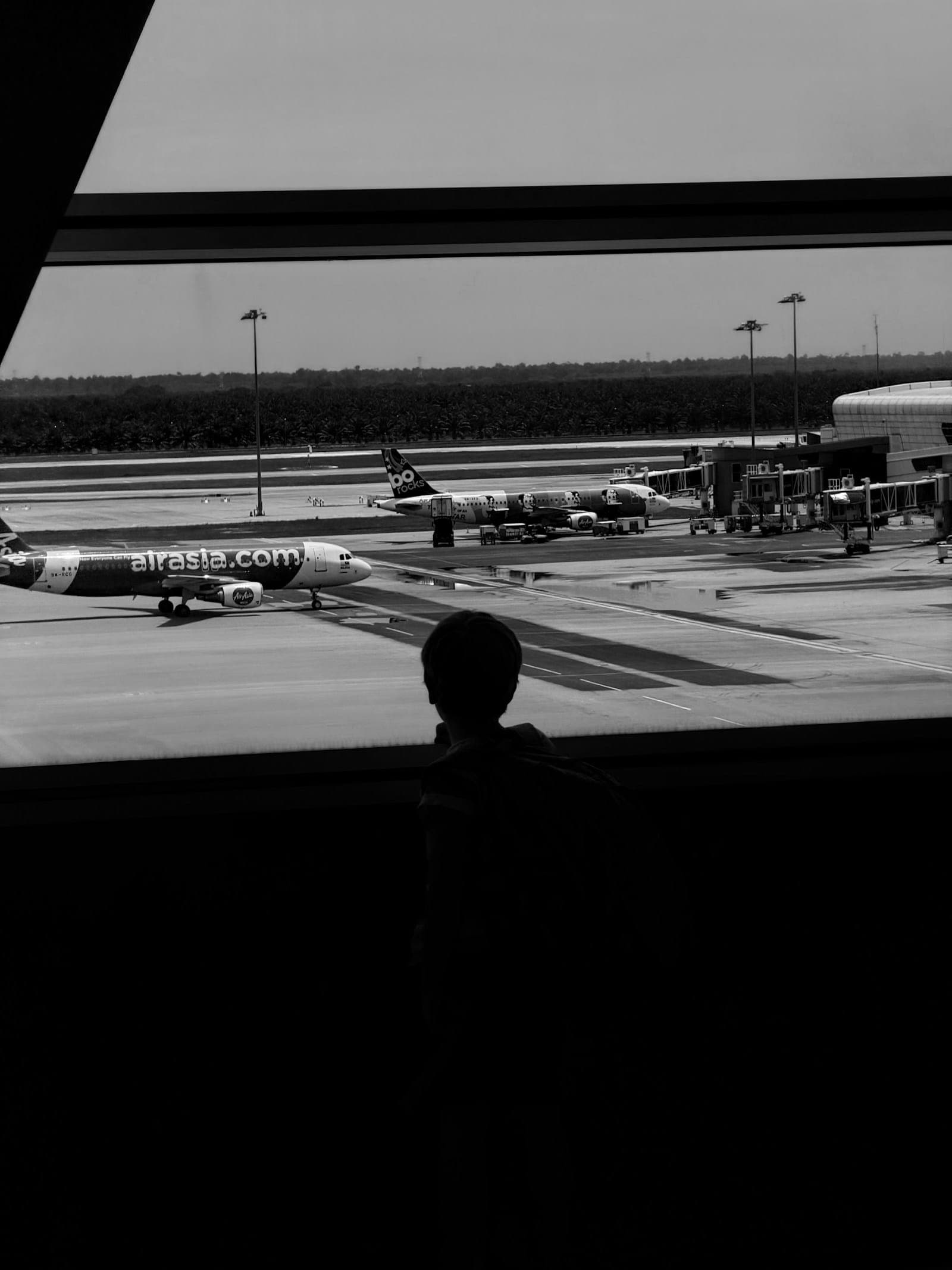 Silhouette of a child at an airport window watching planes on the tarmac, illustrating an AP English Language rhetorical analysis of a memoir about a boy leaving China to join his parents in Canada