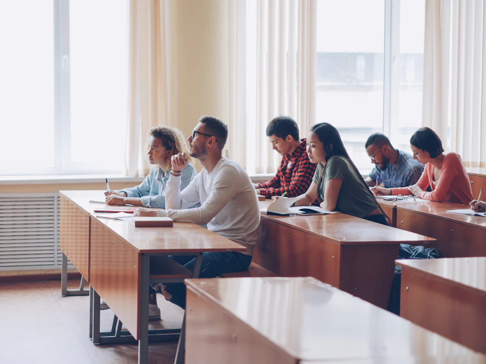 A teacher at the front of a high school classroom, students at their desks